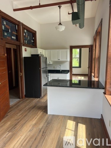 A kitchen with a black refrigerator and wooden floors.
