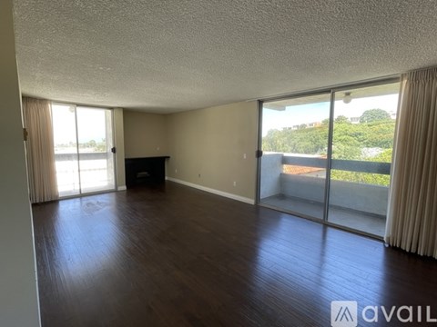 A spacious room with wooden floors and sliding glass doors leading to a balcony.