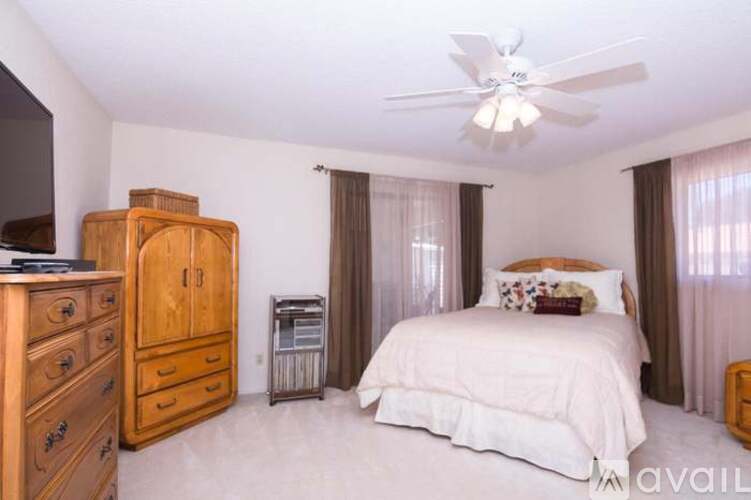 A bedroom with a large bed, a wooden dresser, and a ceiling fan.