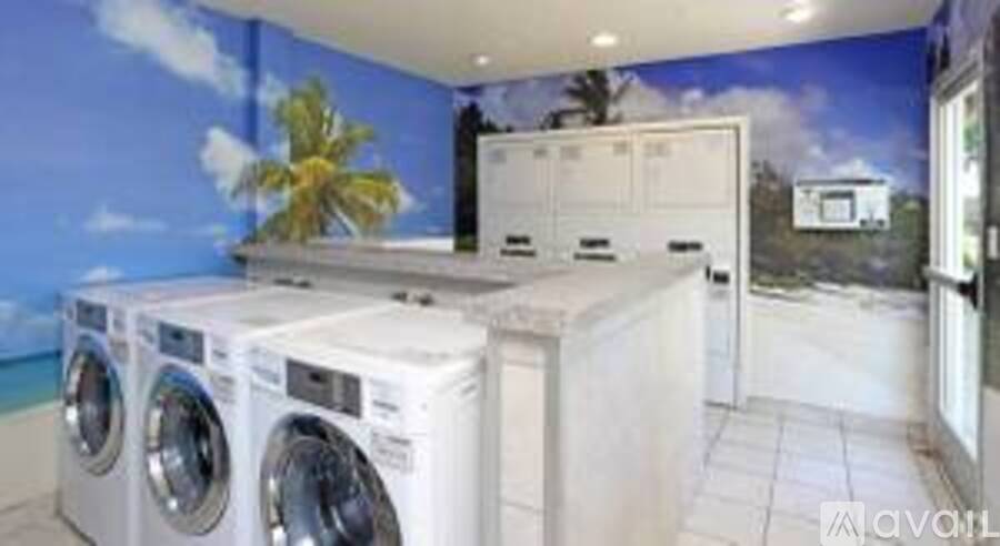 A wall mural of a beach scene is behind a row of washing machines.