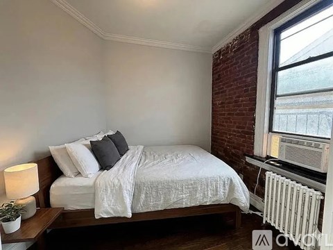 A bedroom with a white bed and a window with blinds.