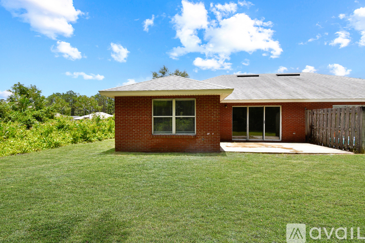 A house with a red brick exterior and a grey roof is surrounded by a grassy lawn.