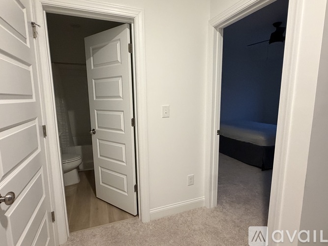 A white door is open to a bedroom with a bed and a white wall.