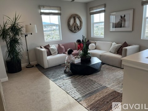 A woman is kneeling on a rug in a living room with a couch, a plant, and a wreath on the wall.