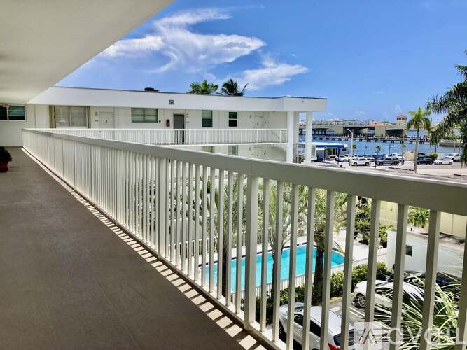 A white building with a balcony overlooking a pool and a parking lot.