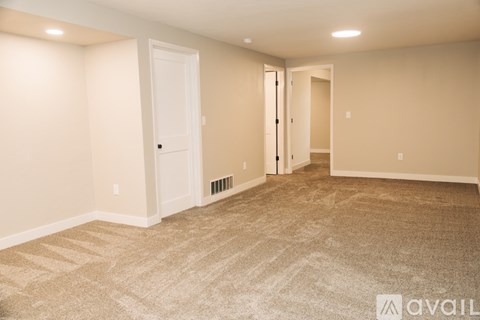 A spacious room with beige carpeting and white walls.
