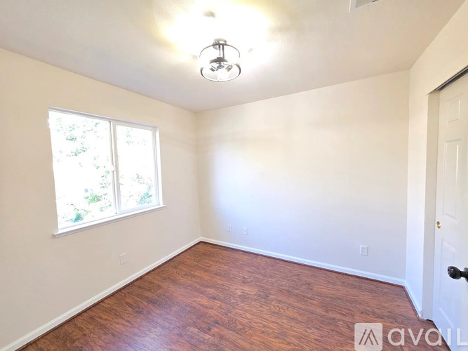 A room with wooden floors and a window with a view of trees.