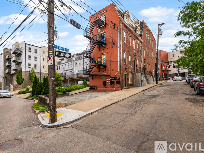 A street view of a residential area with a red brick building on the right and a white car parked on the left.