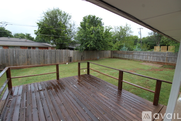A wooden deck with a metal railing is surrounded by a fence and trees.