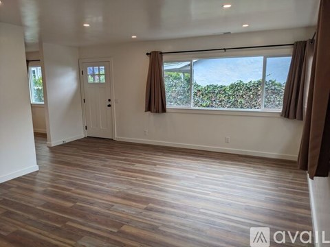 A room with wooden flooring and a window overlooking a hedge.