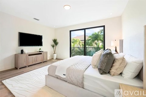 A bedroom with a large bed, a flat screen TV, and a view of a fence and trees outside the window.