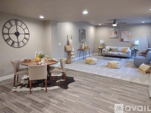 A living room with a dining table set up with chairs and a clock on the wall.