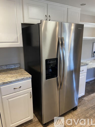 A stainless steel refrigerator with a black panel on the door stands in a kitchen.