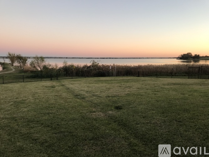 A grassy field with a fence and a body of water in the distance.