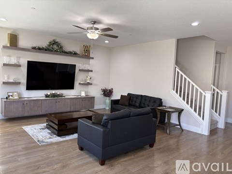 A living room with a black couch, a wooden coffee table, and a television on a wall with a garland.