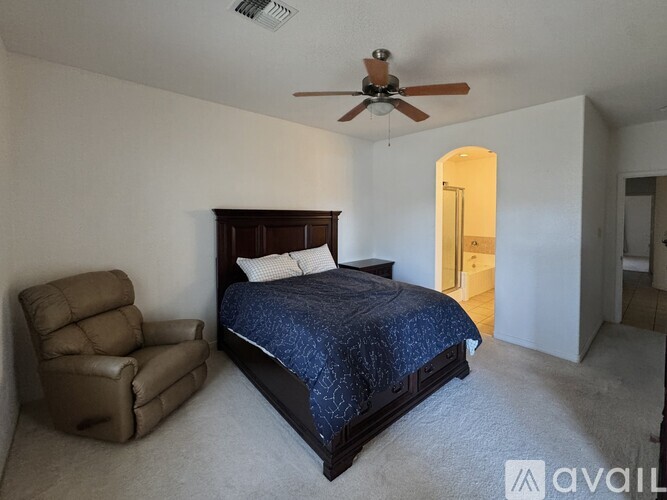 A bedroom with a bed, chair, and ceiling fan.
