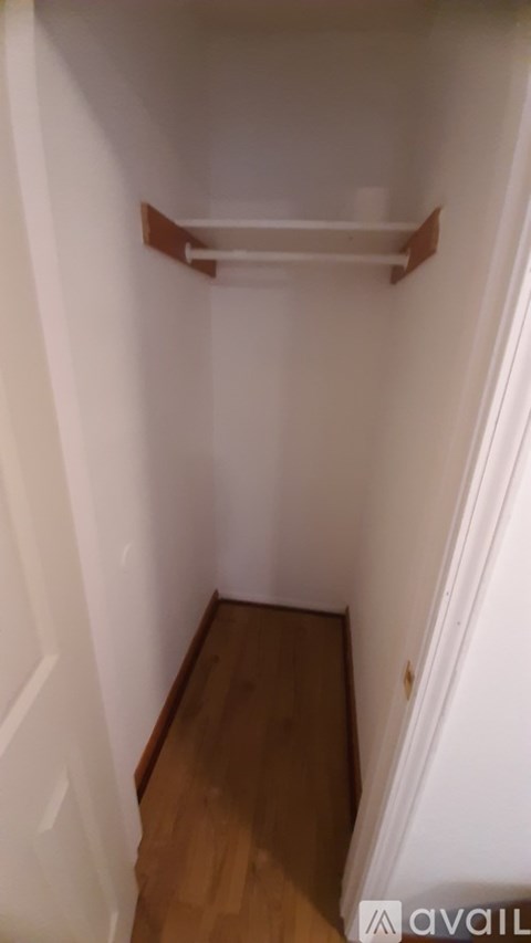 A white hallway with a wooden floor and a shelf on the wall.
