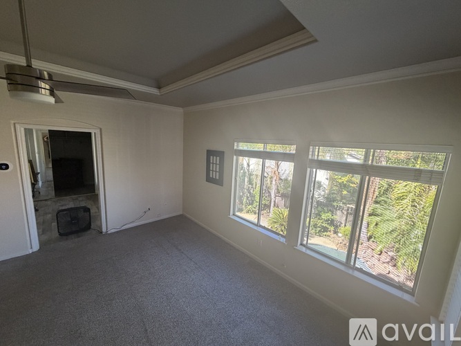 A room with a grey carpet and a window showing trees outside.