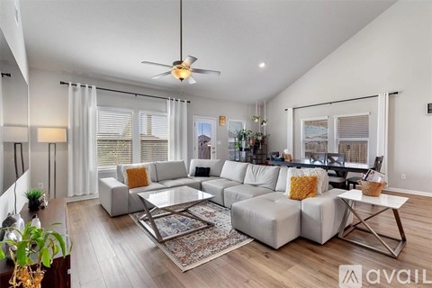 A spacious living room with a white sofa set and a rug on the floor.