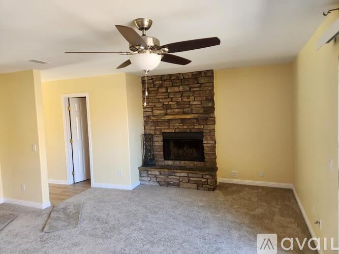 A living room with a stone fireplace and a ceiling fan.