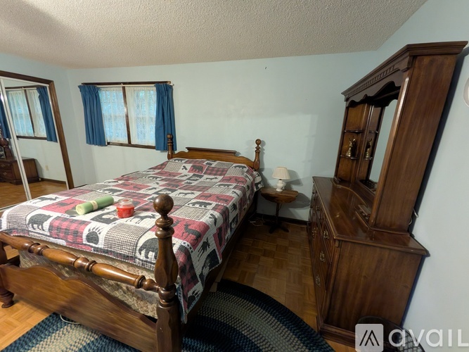 A bedroom with a bed, wooden dresser, and a window with blue curtains.