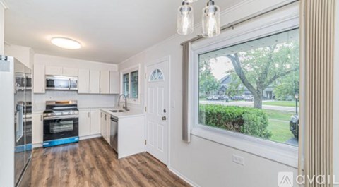 A kitchen with white cabinets and a large window overlooking a tree.