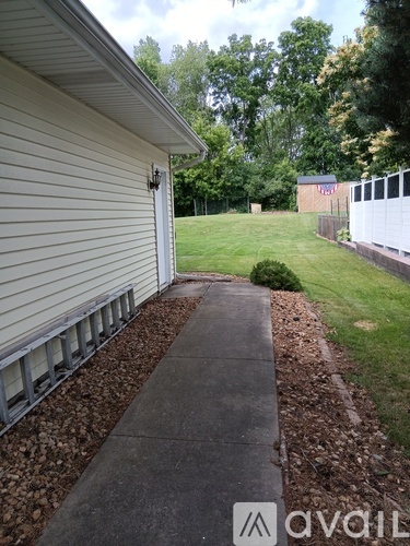 A house with a white siding and a grey roof with a concrete walkway leading to a garage.