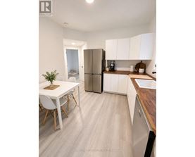 A white kitchen with a refrigerator, sink, and dining table.