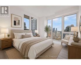 A bedroom with a large bed, a nightstand, a chair, and a view of the city.
