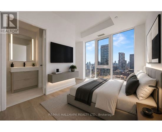 A bedroom with a large bed and a city view through the windows.