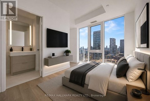 A bedroom with a large bed and a city view through the windows.