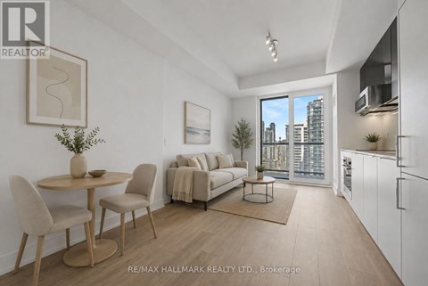 A well-lit, modern living room with a dining table and chairs, a sofa, and a kitchen area with white cabinets.