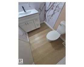A white toilet sits in a bathroom with a marble wallpapered wall.