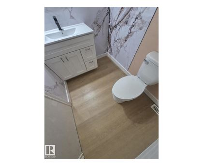 A white toilet sits in a bathroom with a marble wallpapered wall.