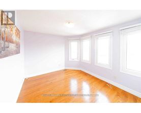 A room with wooden floors and white walls with three windows.