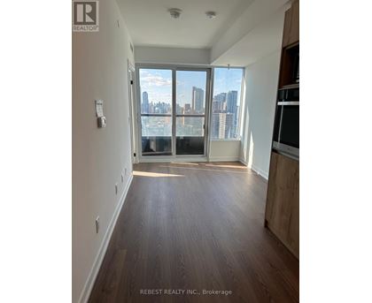 A spacious room with wooden flooring and a view of the city through large windows.