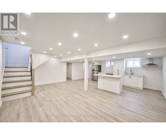 A spacious room with a staircase and a kitchenette.