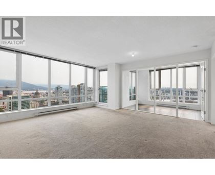 A large, empty room with a view of the cityscape outside the windows.