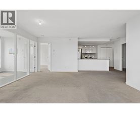 A spacious, empty living room with a kitchen in the background.