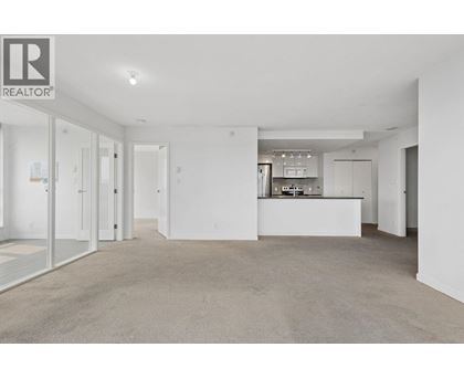 A spacious, empty living room with a kitchen in the background.
