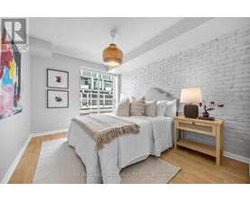A bedroom with a white brick wall and a bed with a white comforter.