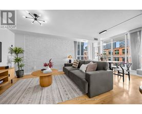 A living room with a grey couch, a wooden coffee table, and a large window with a view of the city.