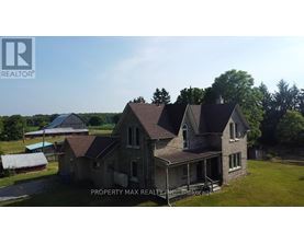 A large, two-story house with a porch is surrounded by greenery and a clear sky.