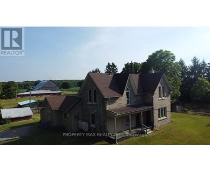A large, two-story house with a porch is surrounded by greenery and a clear sky.