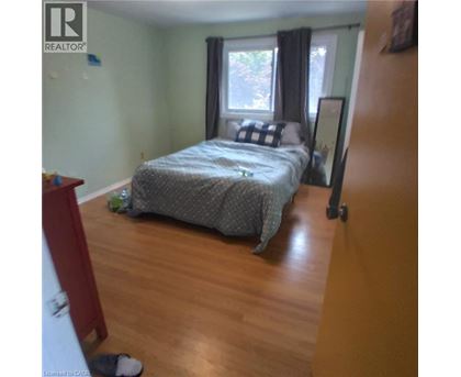 A bedroom with a bed, a window with curtains, and a wooden floor.