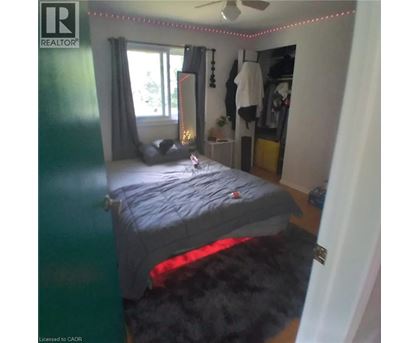 A bedroom with a bed, a window with curtains, a rug, a ceiling fan, and a coat hanging on the wall.