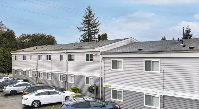 A grey building with a green sign on the side and cars parked in front.
