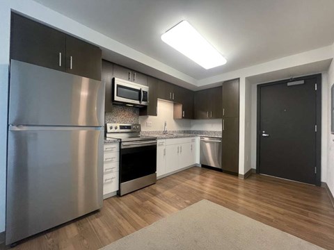 A modern kitchen with a stainless steel refrigerator and wooden flooring.