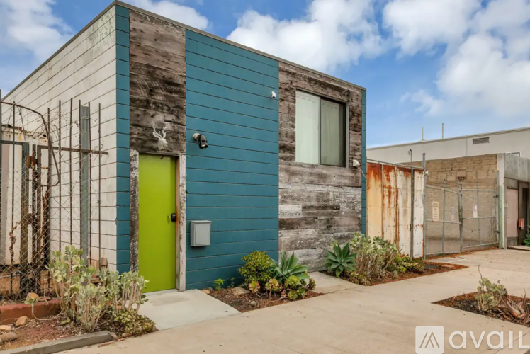 A blue and grey house with a green door and a small garden in front.