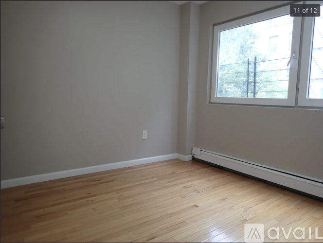 A room with wooden flooring and a window showing a fence and trees outside.